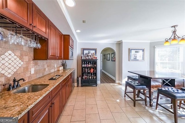 kitchen with stainless steel microwave, decorative light fixtures, sink, decorative backsplash, and light stone counters