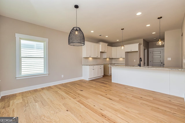 kitchen with pendant lighting, light hardwood / wood-style flooring, light stone countertops, and white cabinets