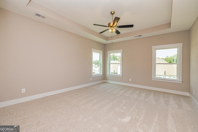 carpeted empty room with ceiling fan, a raised ceiling, and a wealth of natural light