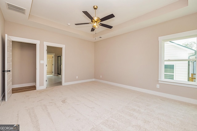 unfurnished bedroom featuring ceiling fan, a raised ceiling, carpet floors, and multiple windows