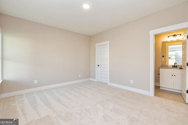 unfurnished bedroom featuring light carpet, sink, and ensuite bathroom