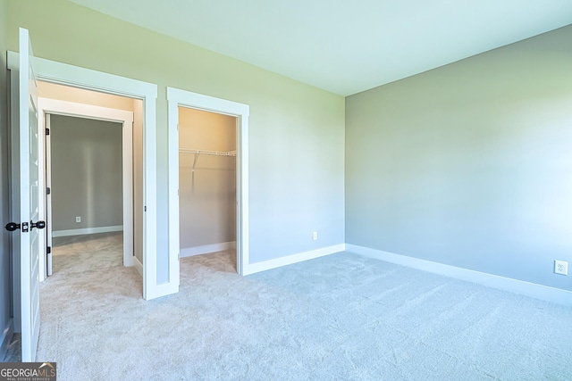 unfurnished bedroom featuring light carpet, a walk in closet, and a closet