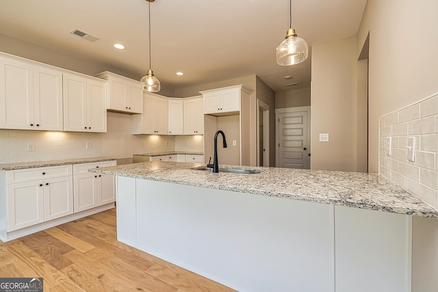 kitchen with sink, white cabinets, backsplash, hanging light fixtures, and light stone counters