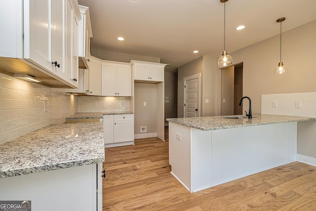 kitchen with decorative light fixtures, sink, white cabinets, light hardwood / wood-style floors, and light stone counters