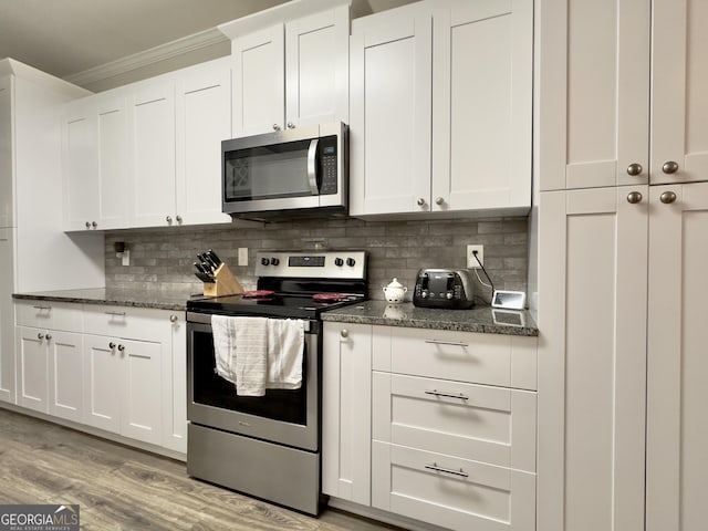 kitchen with crown molding, dark stone countertops, appliances with stainless steel finishes, white cabinets, and backsplash