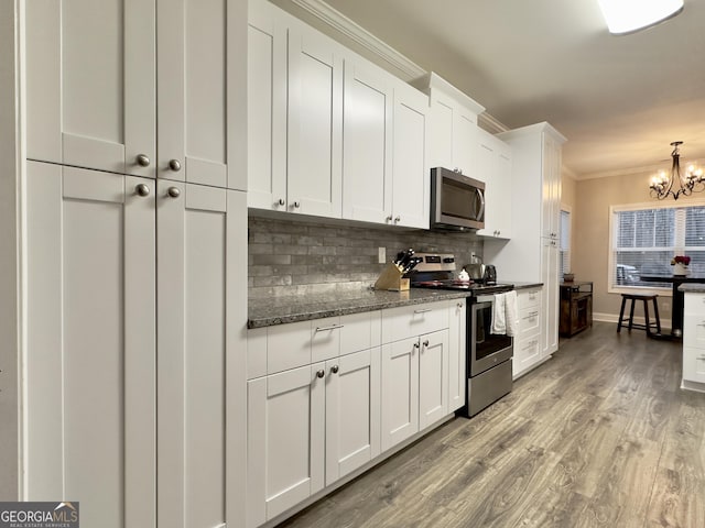 kitchen featuring white cabinetry, a chandelier, ornamental molding, appliances with stainless steel finishes, and stone counters