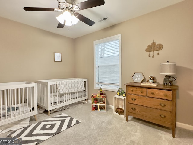 bedroom with a crib, light carpet, and ceiling fan