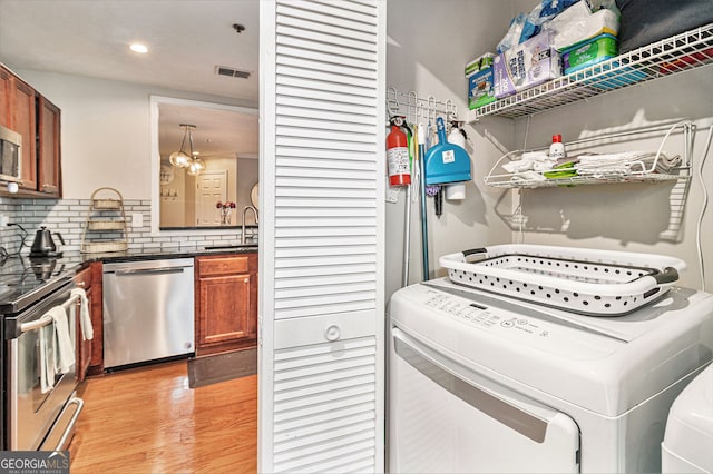 laundry room featuring independent washer and dryer, sink, and light hardwood / wood-style flooring