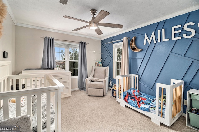 bedroom featuring ceiling fan, a nursery area, ornamental molding, a textured ceiling, and light colored carpet