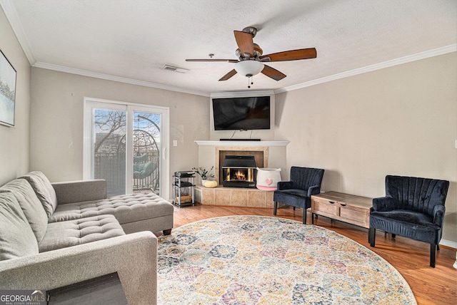 living room featuring crown molding, hardwood / wood-style floors, a tile fireplace, and a textured ceiling