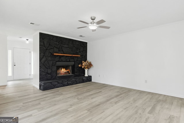 living room with crown molding, a stone fireplace, ceiling fan, and light wood-type flooring