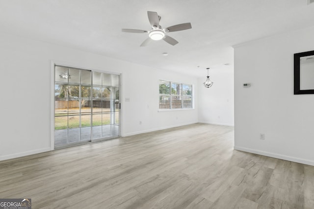 empty room with ceiling fan with notable chandelier and light hardwood / wood-style floors