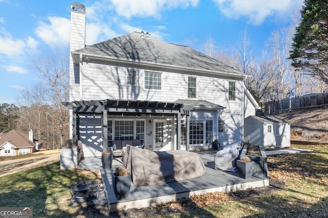 back of property featuring a fire pit, a wooden deck, a pergola, and a storage unit