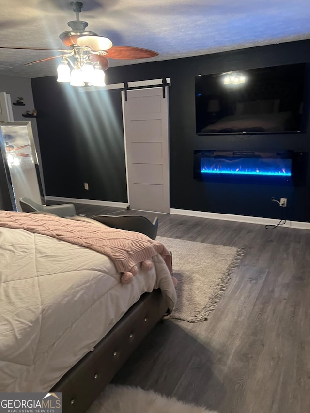 bedroom with ceiling fan, wood-type flooring, a barn door, and a textured ceiling