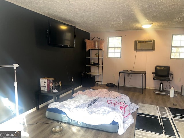 bedroom with hardwood / wood-style floors, a textured ceiling, and an AC wall unit