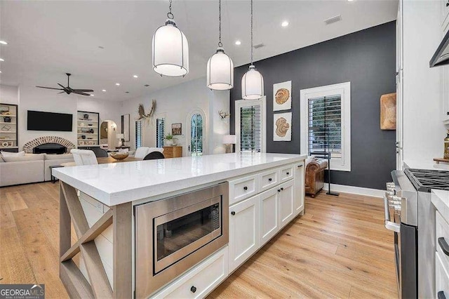 kitchen with appliances with stainless steel finishes, a kitchen island, built in features, white cabinetry, and hanging light fixtures