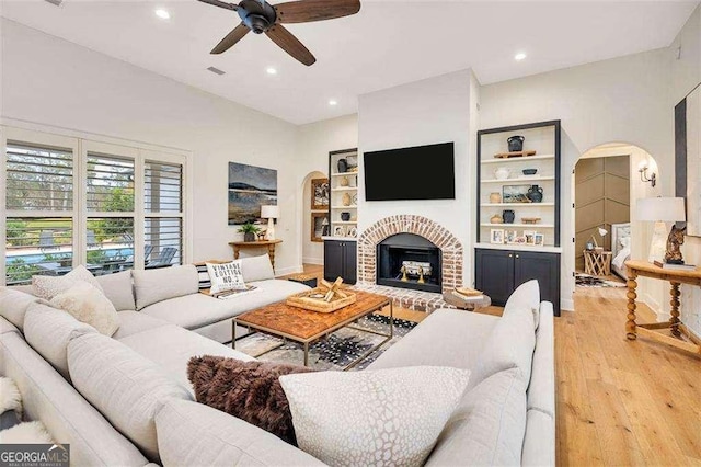 living room with a brick fireplace, hardwood / wood-style floors, ceiling fan, and built in shelves