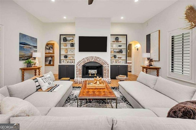 living room with wood-type flooring, a brick fireplace, and built in shelves