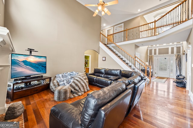 living room featuring wood-type flooring, ornamental molding, ceiling fan, and a towering ceiling