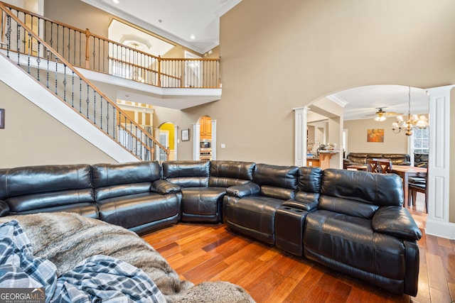 living room with decorative columns, wood-type flooring, a high ceiling, ornamental molding, and an inviting chandelier