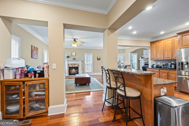 kitchen featuring dark hardwood / wood-style flooring, crown molding, a kitchen breakfast bar, stainless steel refrigerator with ice dispenser, and a brick fireplace