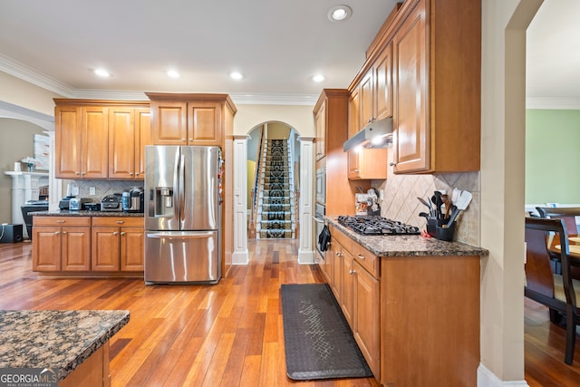 kitchen featuring dark stone countertops, ornamental molding, stainless steel appliances, and light wood-type flooring