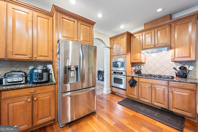 kitchen featuring dark stone countertops, ornamental molding, stainless steel appliances, and light hardwood / wood-style floors