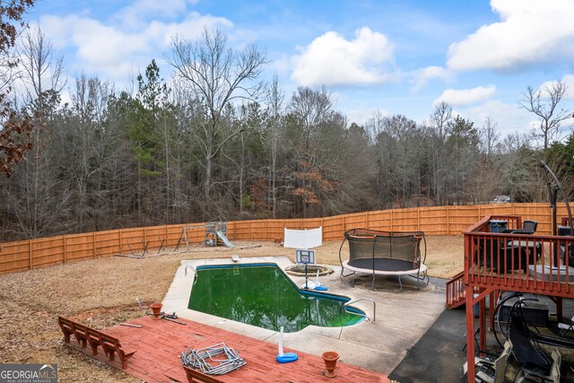 view of pool with a trampoline, a wooden deck, and a diving board