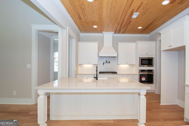 kitchen featuring built in microwave, premium range hood, stainless steel oven, and an island with sink