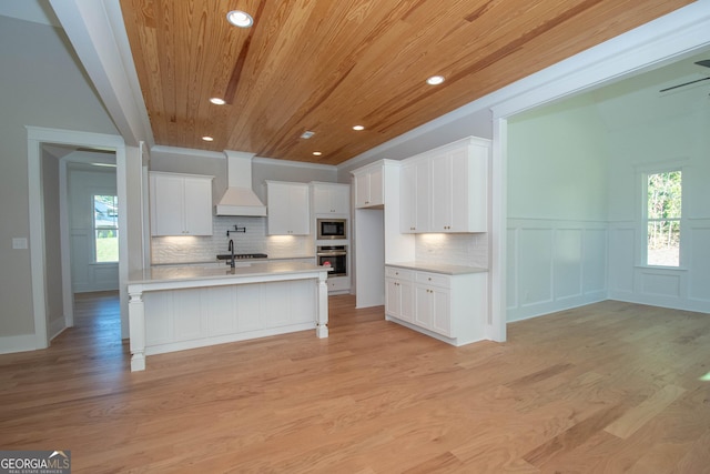 kitchen with white cabinetry, premium range hood, oven, and built in microwave