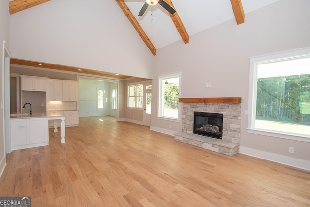 unfurnished living room with sink, light hardwood / wood-style flooring, beam ceiling, high vaulted ceiling, and a fireplace