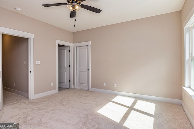 unfurnished bedroom with multiple windows, light colored carpet, and ceiling fan