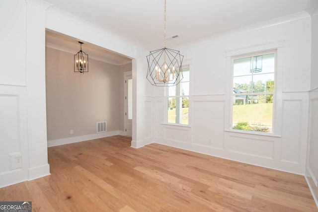 unfurnished dining area with ornamental molding, an inviting chandelier, and light hardwood / wood-style floors