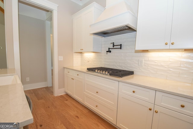 kitchen with stainless steel gas cooktop, tasteful backsplash, light wood-type flooring, custom range hood, and white cabinets