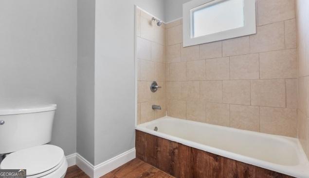 bathroom featuring tiled shower / bath, wood-type flooring, and toilet