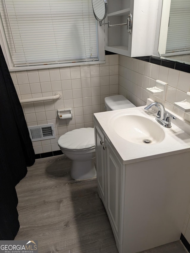 bathroom with tile walls, wood finished floors, toilet, vanity, and backsplash
