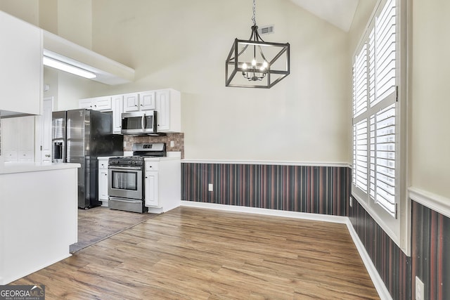 kitchen with lofted ceiling, light hardwood / wood-style flooring, appliances with stainless steel finishes, hanging light fixtures, and white cabinets