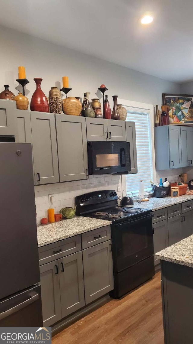 kitchen featuring backsplash, gray cabinets, light hardwood / wood-style flooring, and black appliances