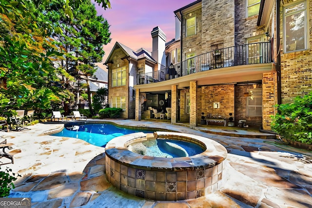 pool at dusk with a patio area and an in ground hot tub