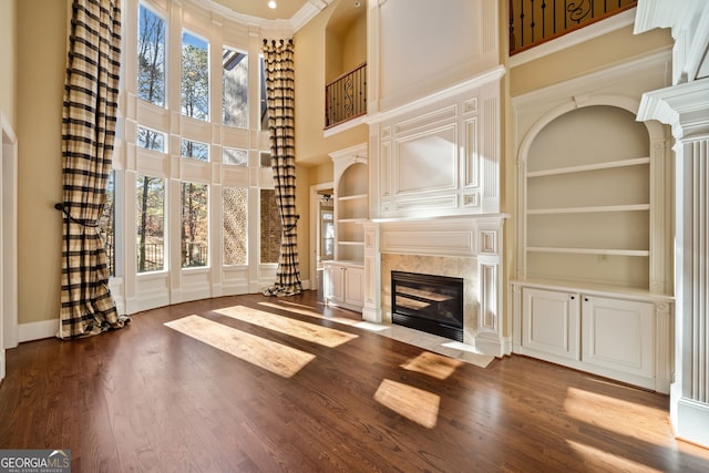 unfurnished living room with plenty of natural light, a towering ceiling, built in features, and a fireplace