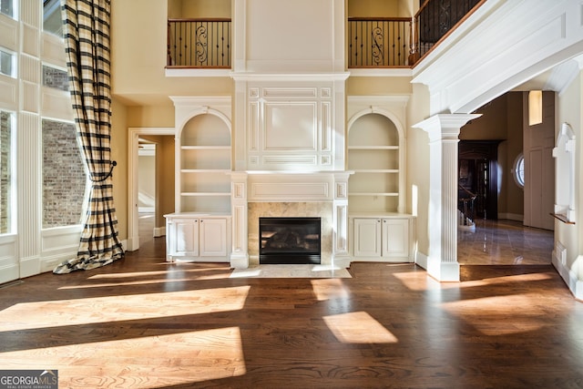 unfurnished living room with a towering ceiling, a fireplace, built in features, and ornate columns