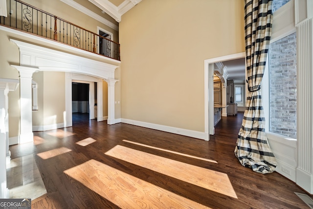 unfurnished living room with ornate columns, crown molding, dark wood-type flooring, and a high ceiling