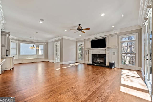 unfurnished living room with ceiling fan with notable chandelier, light hardwood / wood-style flooring, ornamental molding, and a healthy amount of sunlight