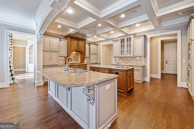 kitchen featuring beam ceiling, sink, an island with sink, and decorative backsplash