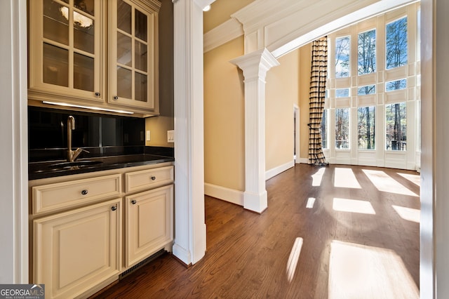 bar featuring sink, cream cabinets, dark wood-type flooring, and ornate columns