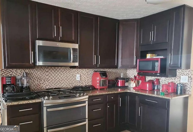 kitchen with dark brown cabinetry, appliances with stainless steel finishes, light stone counters, and decorative backsplash