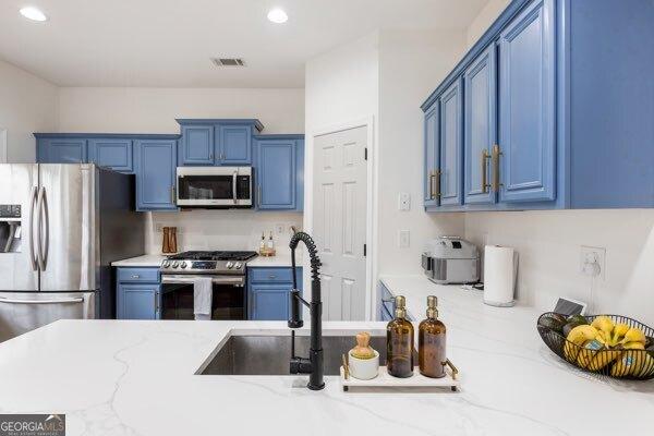 kitchen featuring light stone counters, stainless steel appliances, and blue cabinets