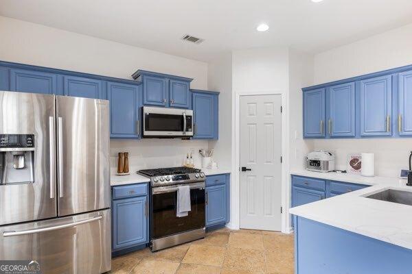 kitchen with blue cabinetry, stainless steel appliances, light stone countertops, and sink