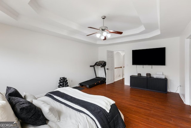 bedroom with a raised ceiling, wood-type flooring, and ceiling fan