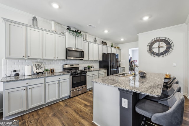 kitchen featuring appliances with stainless steel finishes, sink, a kitchen breakfast bar, light stone countertops, and a center island with sink